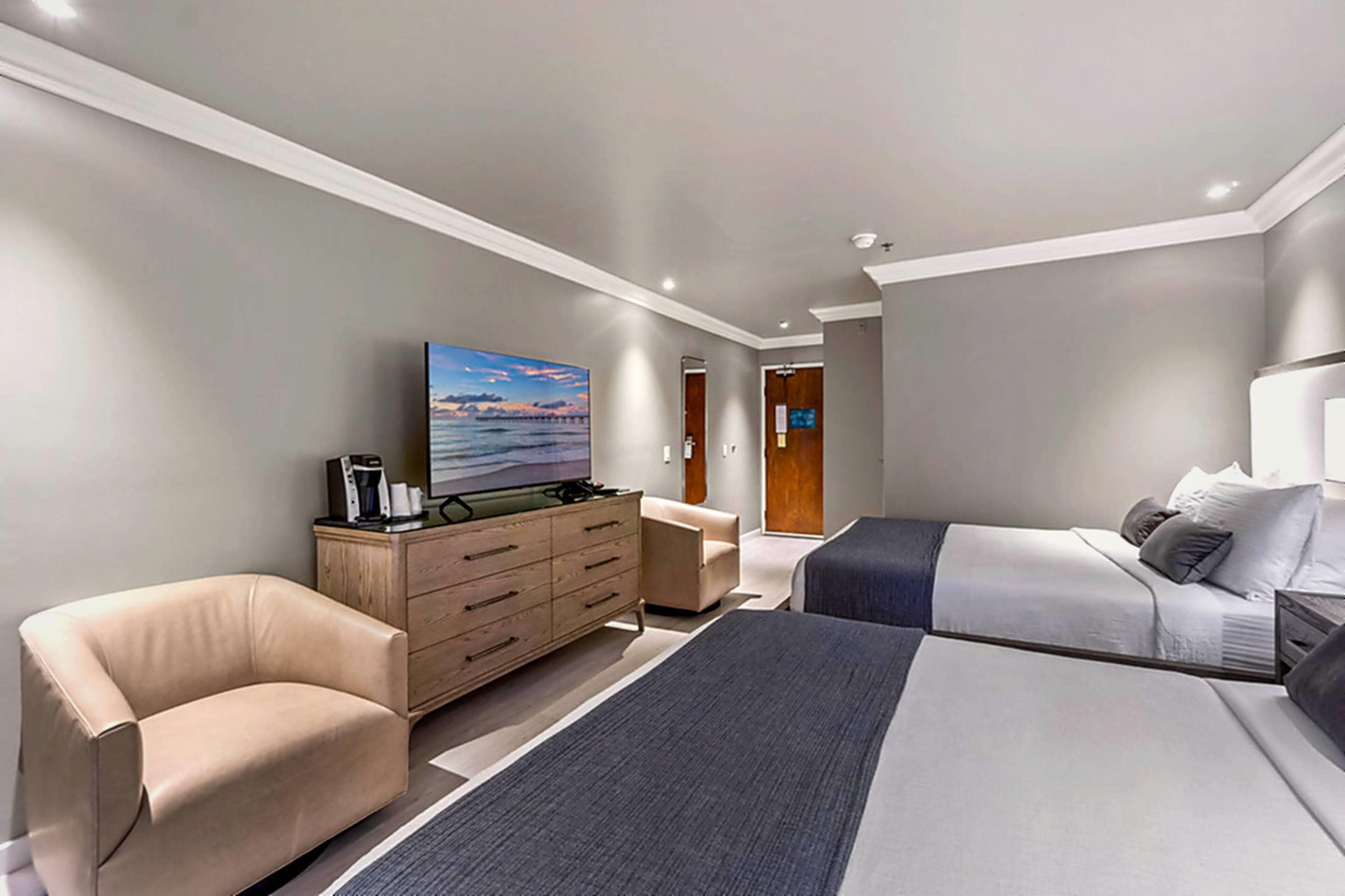 A modern hotel room with a large bed, a sofa, a TV, and a dresser.
