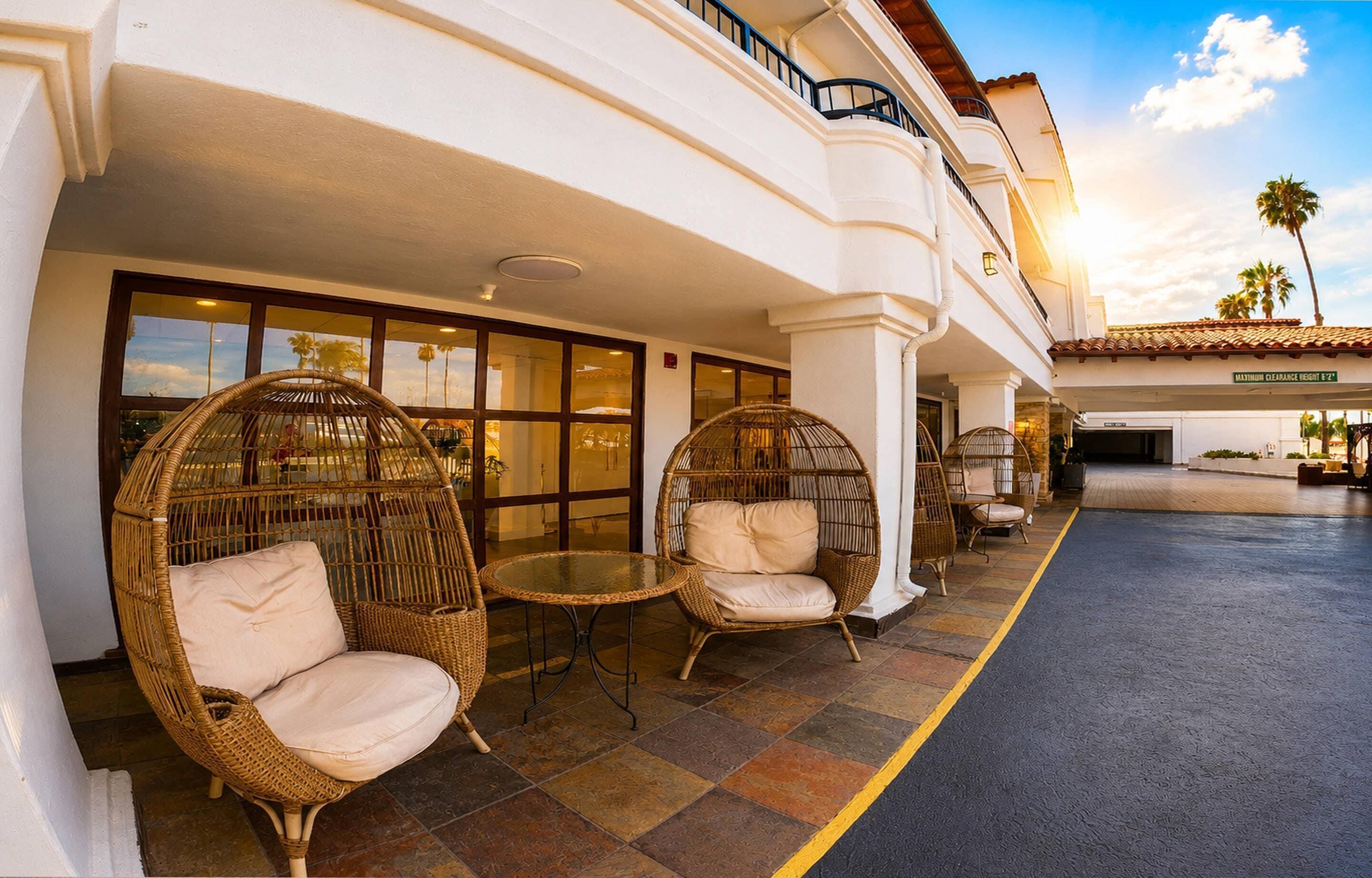 Entrada de un hotel con sillas y mesas de mimbre, un corredor cubierto y una vista despejada de la arquitectura del edificio.