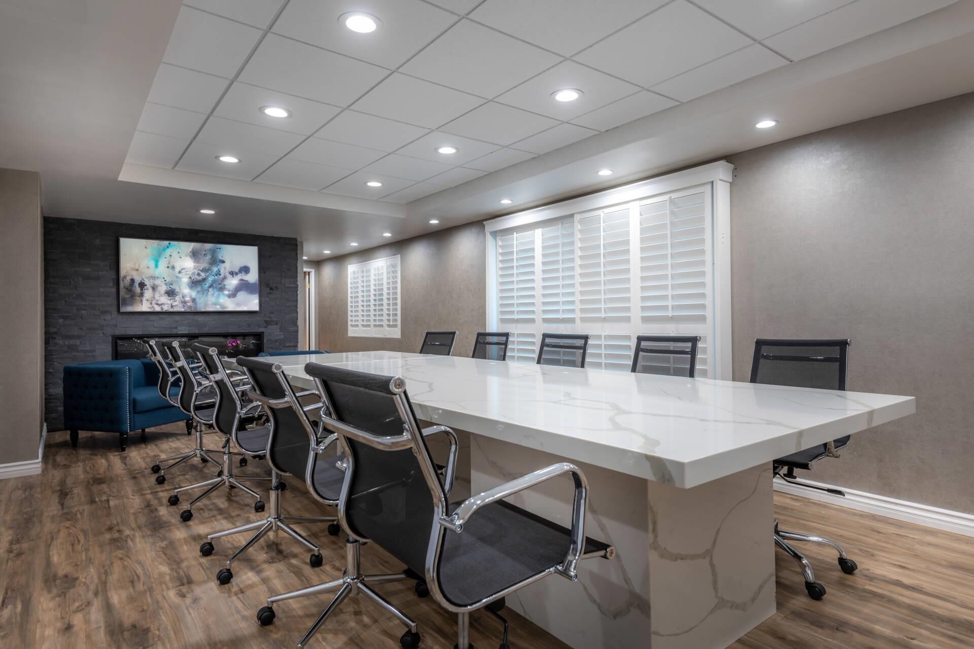 A conference room with a long table, chairs, a fireplace, and a large window with blinds.