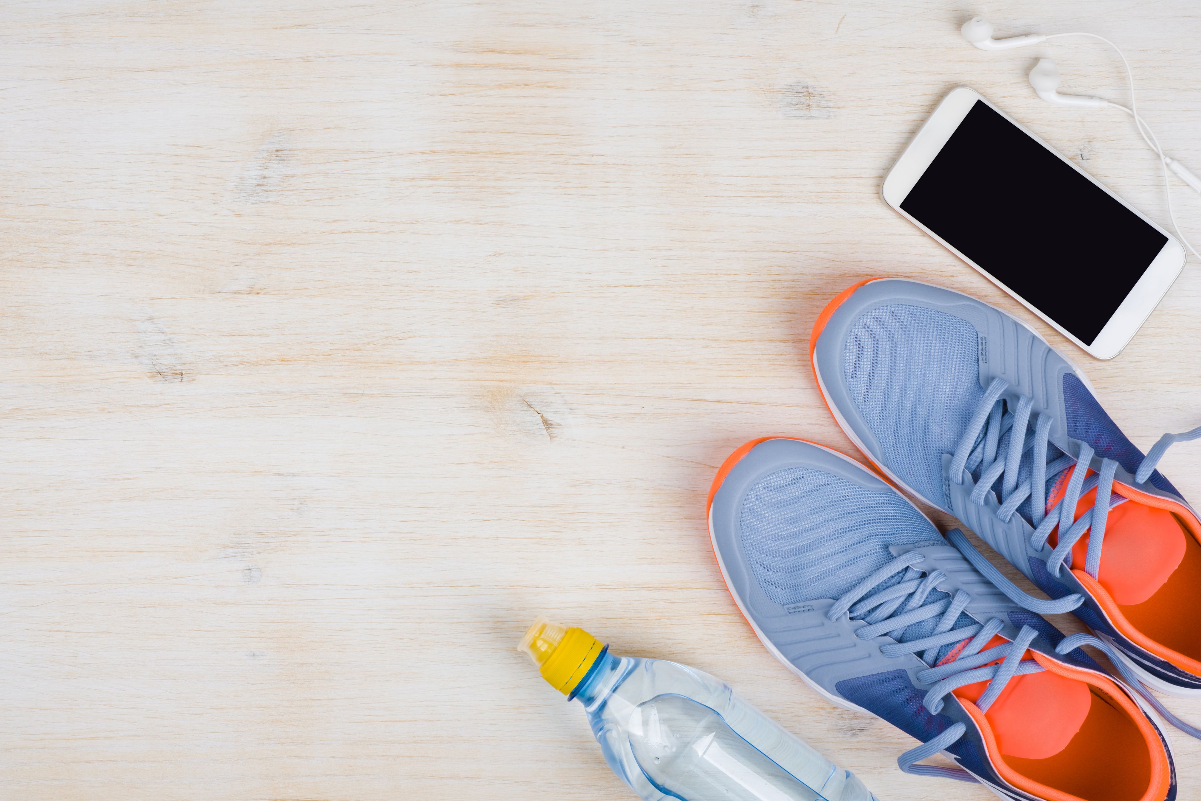 A pair of blue and orange sneakers, a smartphone, and a water bottle on a wooden surface.