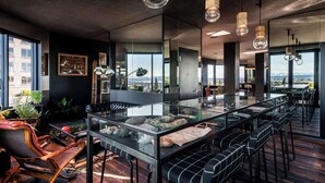 A modern bar area with a glass-top table, bar stools, and pendant lighting. - Graduate by Hilton Seattle (Seattle)