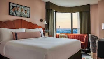 Habitació d'hotel amb un llit gran, un butaca vermella, un escriptori i vista a la ciutat.