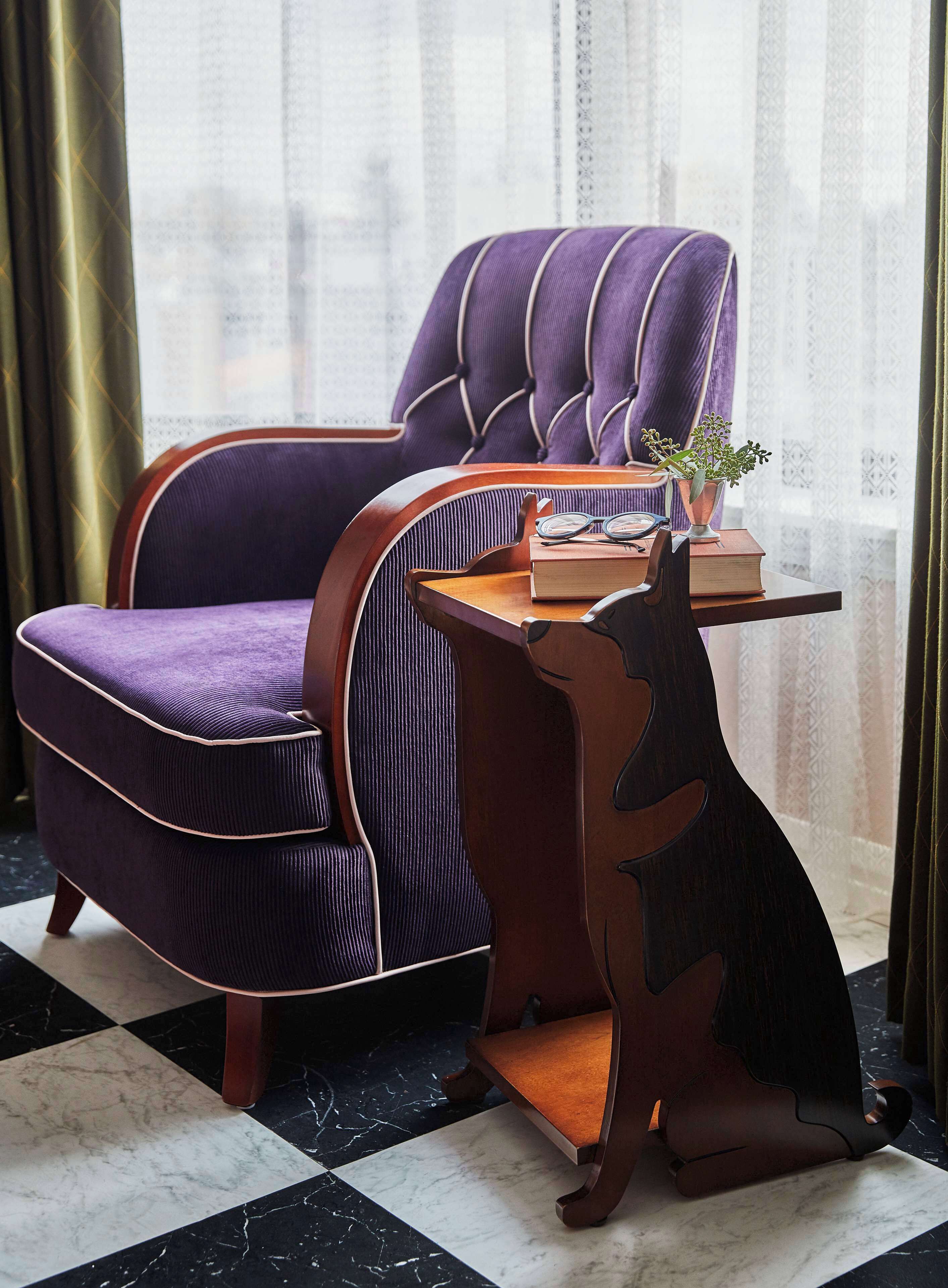 A purple upholstered chair with a wooden side table, a book, and a small plant.