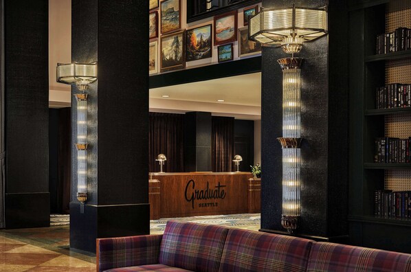 A lobby with a reception desk labeled "Graduate Seattle," tall columns with wall sconces, a patterned carpet, and a plush sofa.