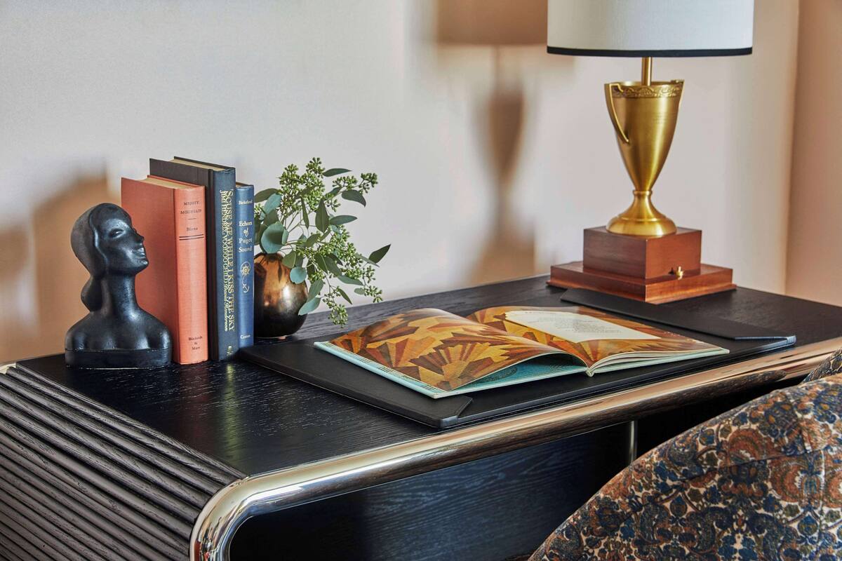 Une table de chevet bien rangée, avec des livres, un buste décoratif, une petite plante et une lampe.