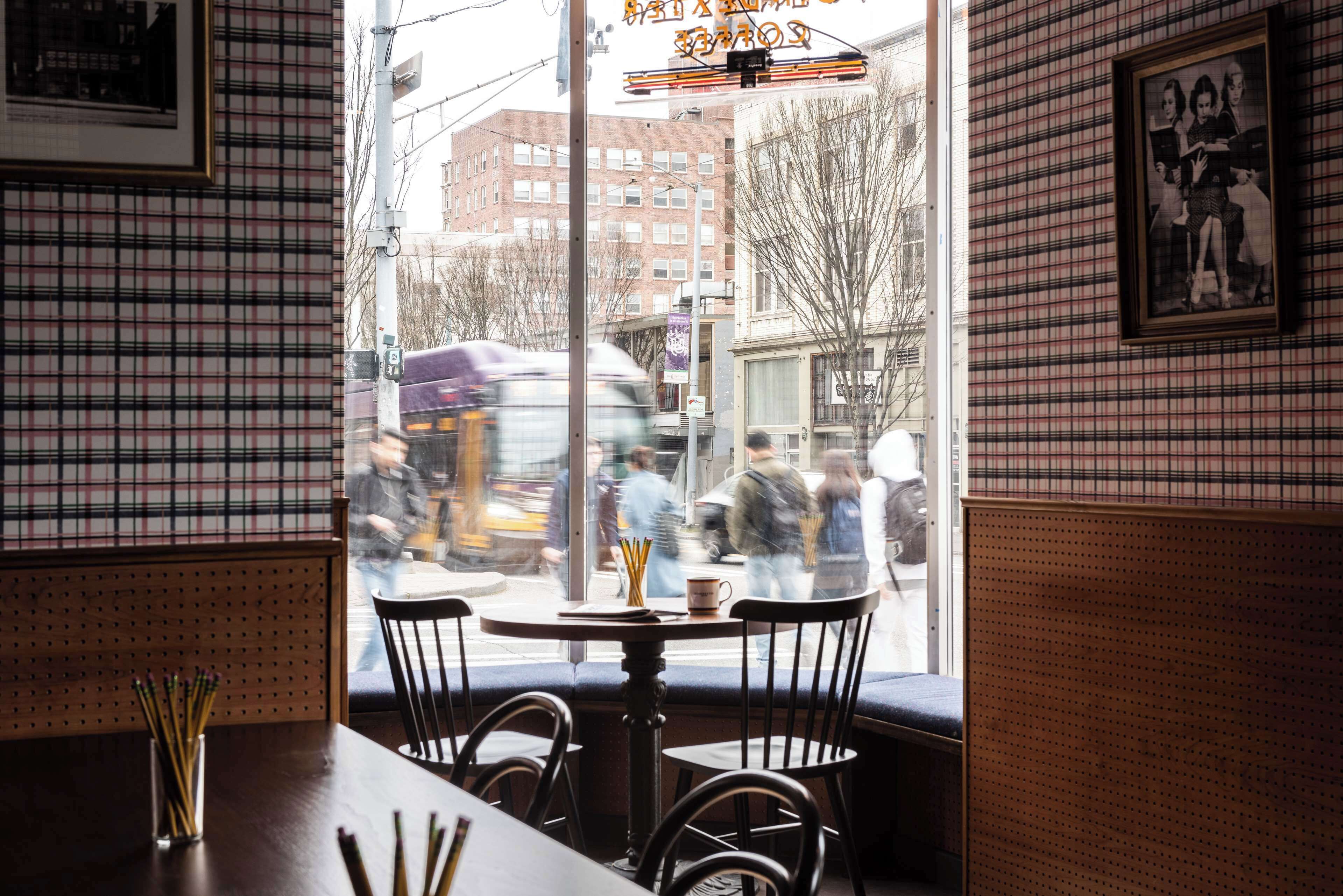 A restaurant interior with a window view of the street, a table with chairs, and a wall with a checkered pattern.