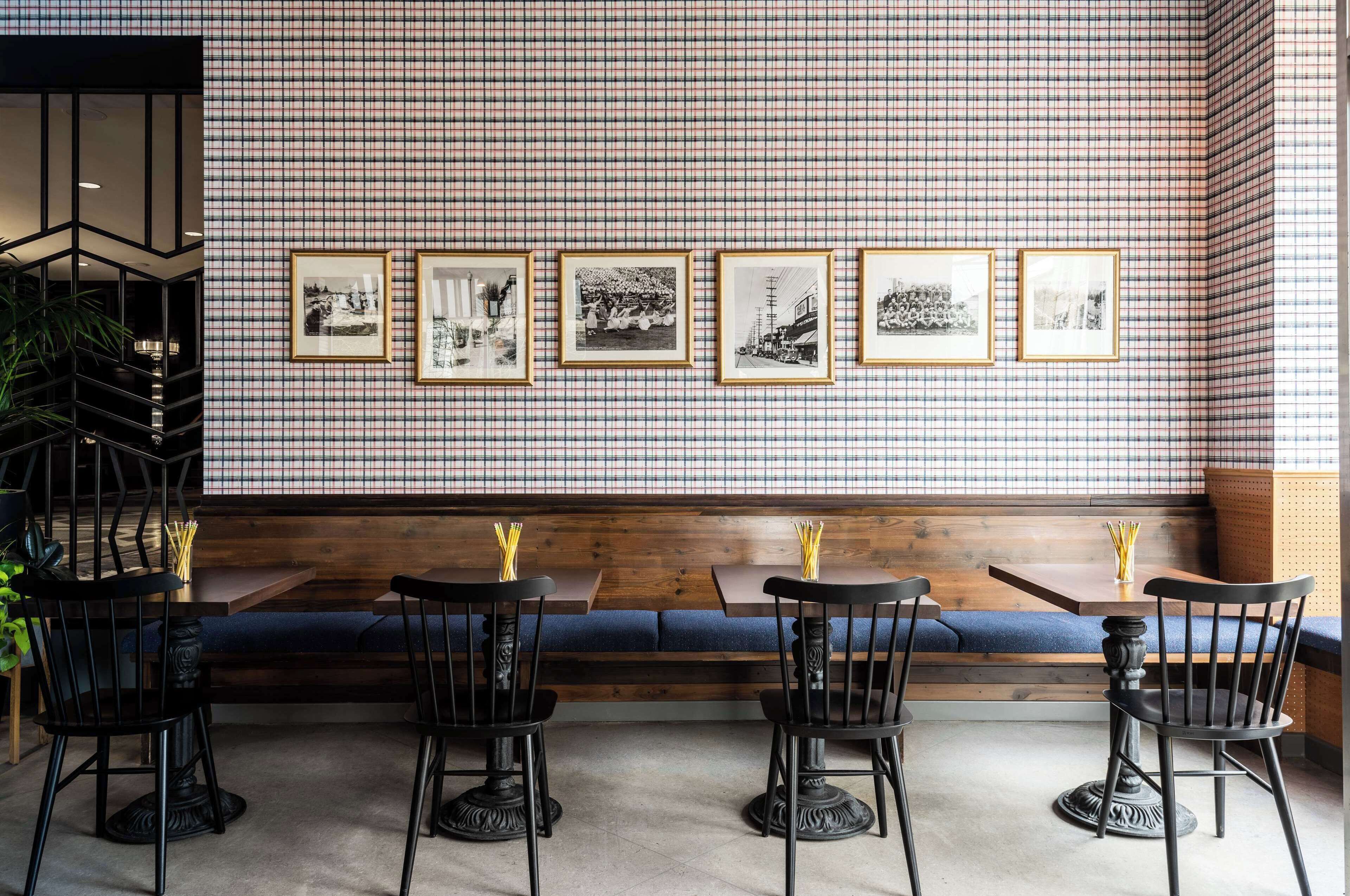 A restaurant with a checkered wall, framed pictures, wooden benches, and black chairs.