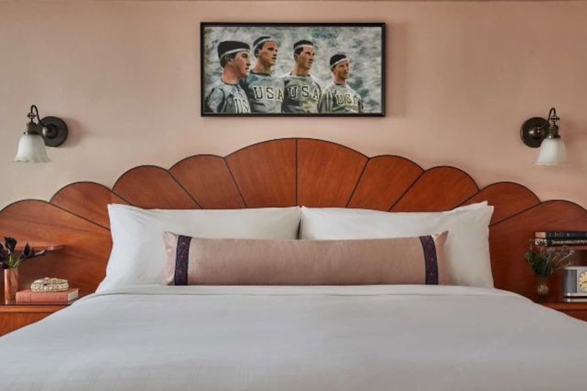 Una cama bien hecha con cabecera, un cuadro enmarcado encima y mesitas de noche con lámparas.
