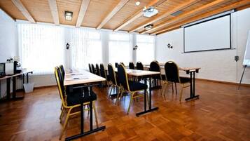 A conference room with wooden floors, a long table with chairs, a projector screen, and a whiteboard.