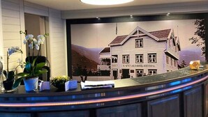 Una zona de recepció amb un mostrador corbat, plantes en testos i un quadre amb una casa a la paret.