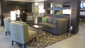 A modern hotel lobby with a sofa, armchairs, a coffee table, and a TV.