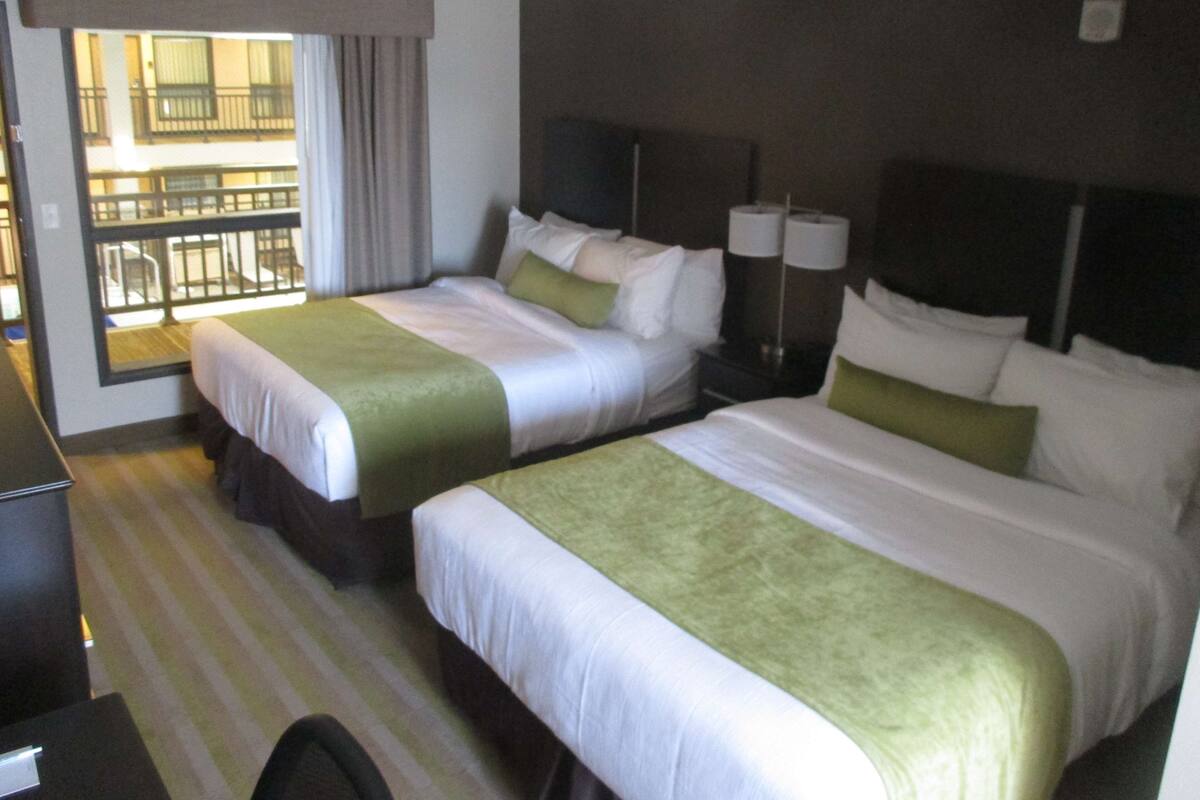 A hotel room with two beds, a desk, and a window with a view of a building.