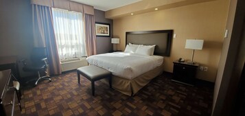 Una habitación de hotel con una cama grande, un escritorio, una silla, una mesita de noche con lámpara y una ventana con cortinas.