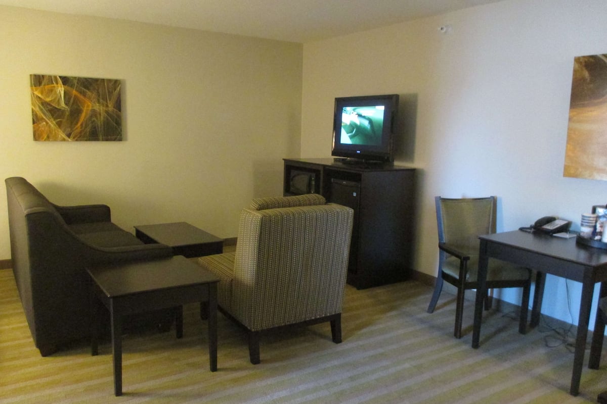 A hotel room with a sofa, armchair, small table, and a television on a stand.