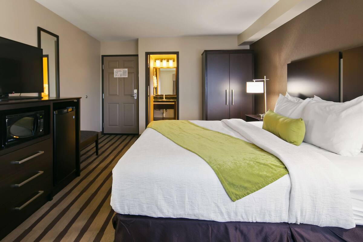 A hotel room with a bed, a television, a desk with a microwave, and a door leading to a bathroom.