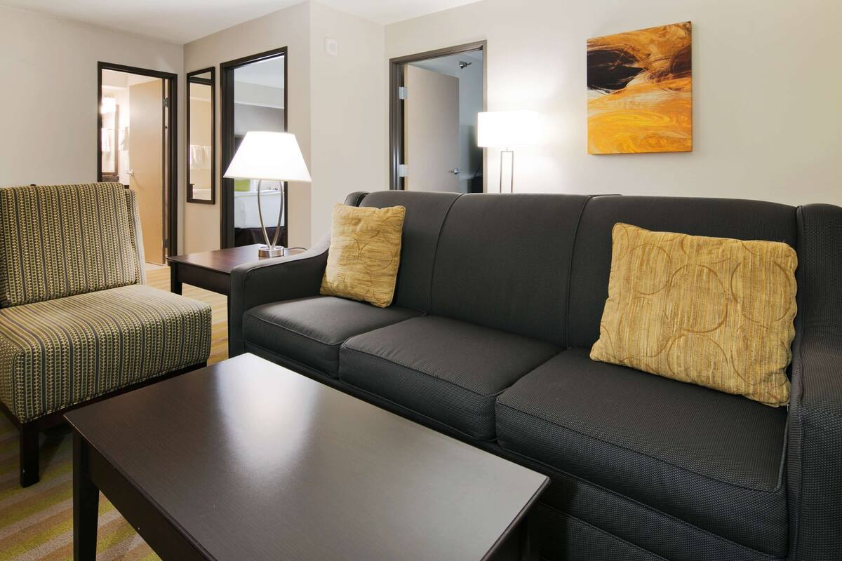 A hotel room with a sofa, armchair, and a table.