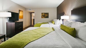 A hotel room with two beds, a TV, a desk, and artwork on the walls.