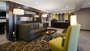 A modern hotel lobby with a sofa, armchairs, a coffee table, and a reception desk.