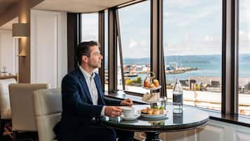 A man seated at a table with a view of the sea and mountains.