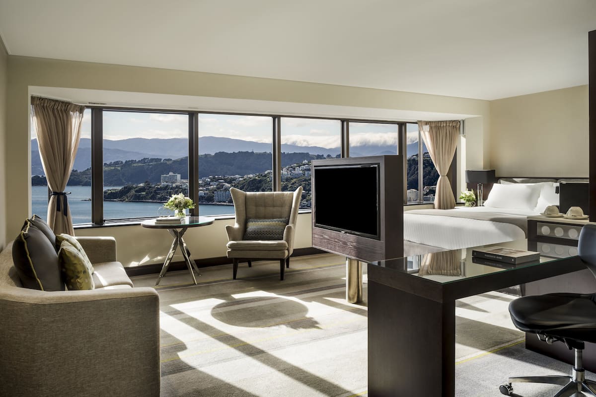 Une chambre d’hôtel avec une grande fenêtre, une télévision, un lit, un bureau et une chaise.