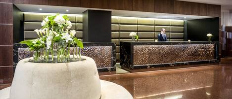 A modern reception area with a marble reception desk, a large vase of white flowers, and a man in a suit standing behind the desk.