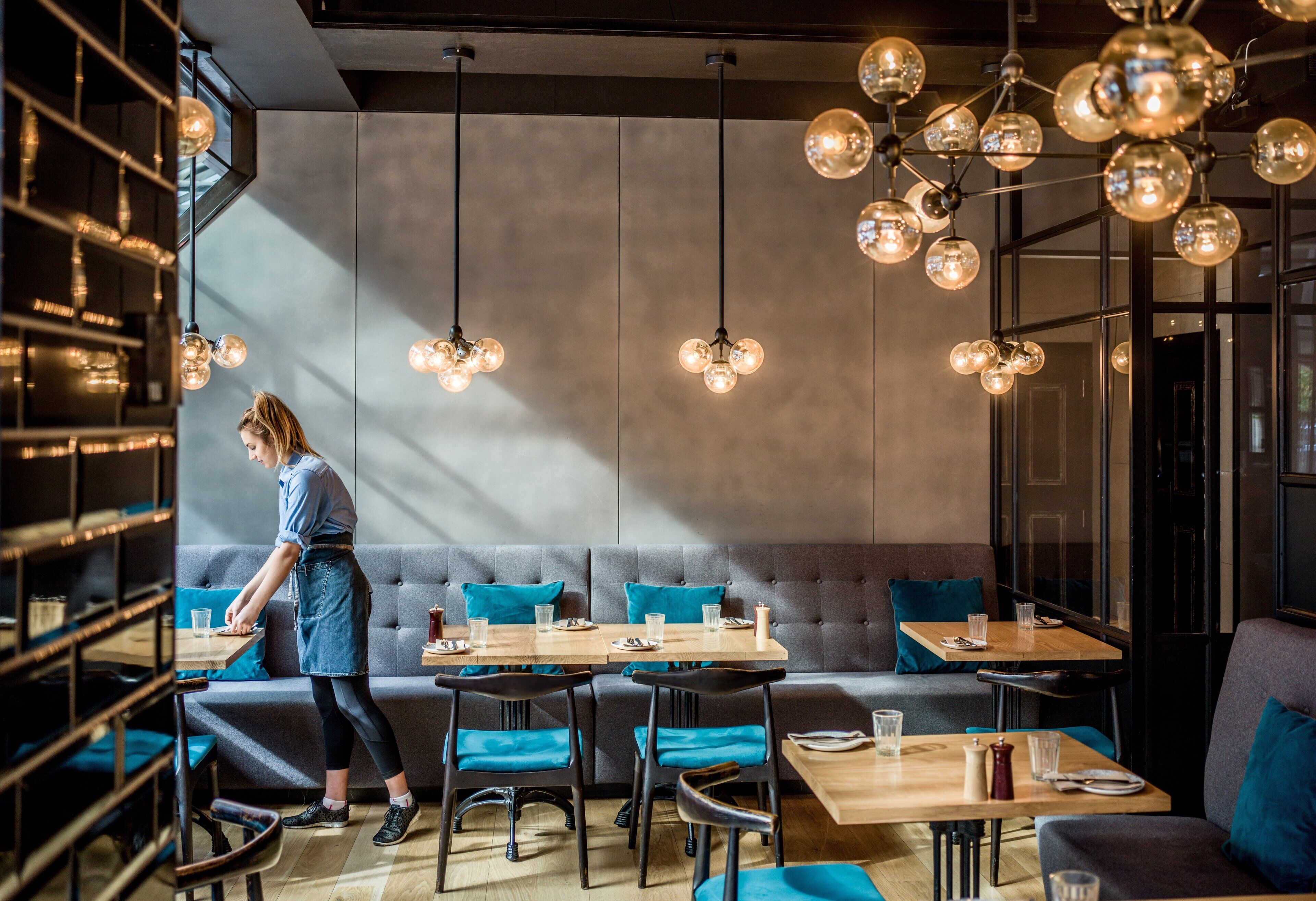 Un interior de restaurante moderno con barra, diferentes disposiciones de asientos y lámparas colgantes esféricas.
