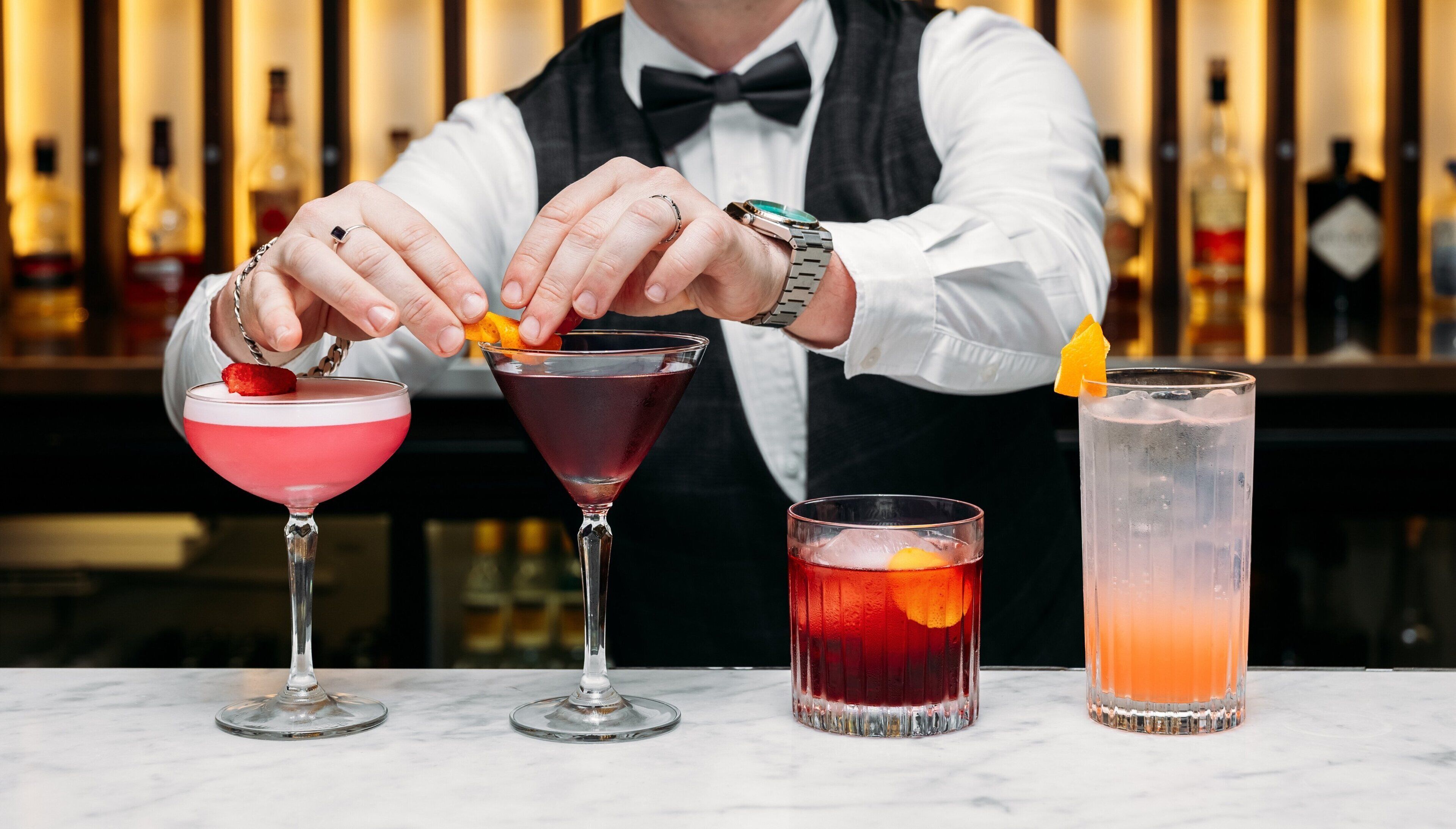 A bartender preparing drinks at a bar with various cocktail glasses and bottles in the background.