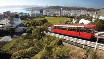 Un funicular rojo con la leyenda 'Wellington Cable Car', que viaja sobre un puente con vegetación y un paisaje urbano al fondo.