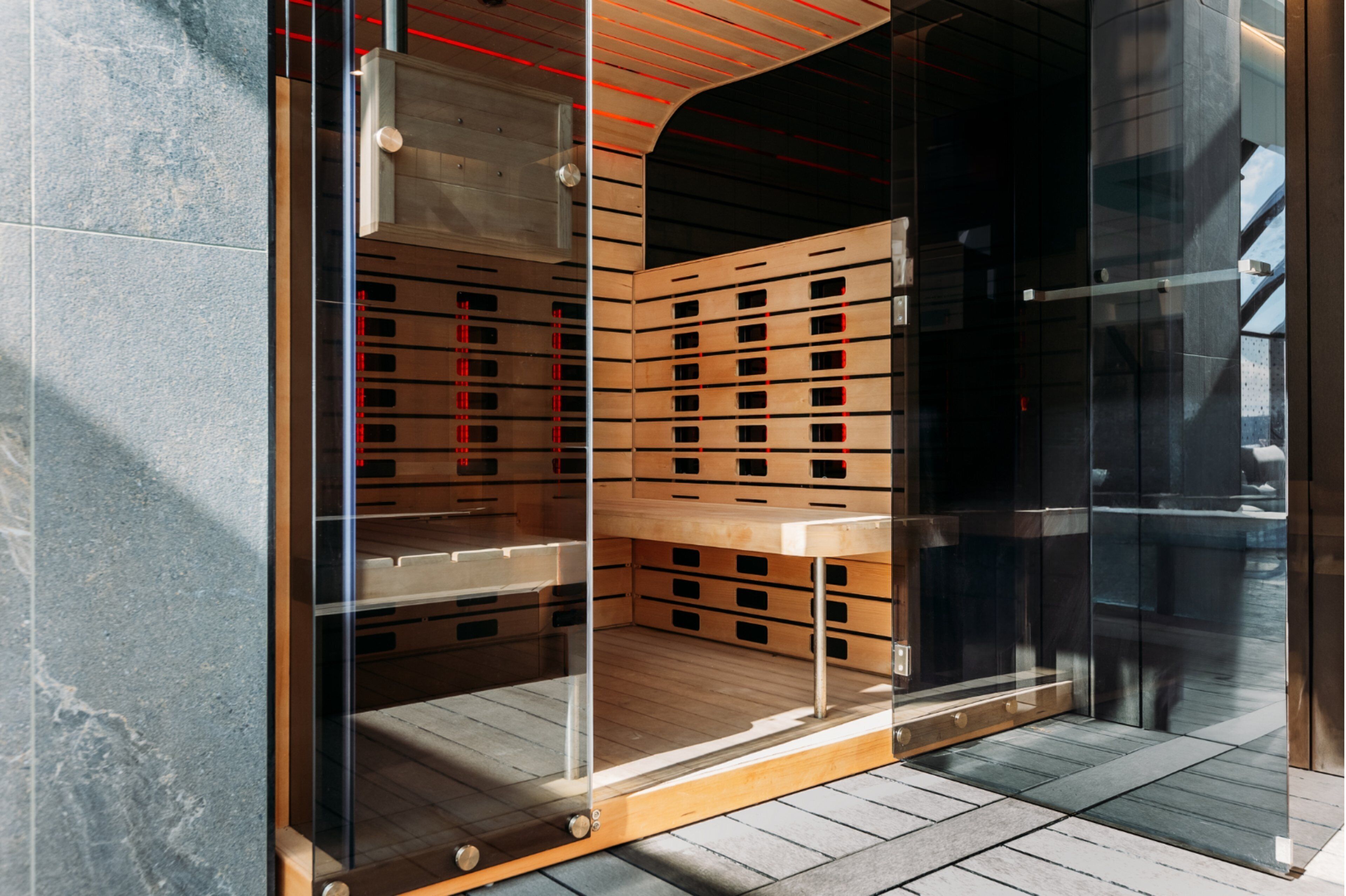 A modern elevator with a transparent glass door, wooden interior, and red lighting accents.
