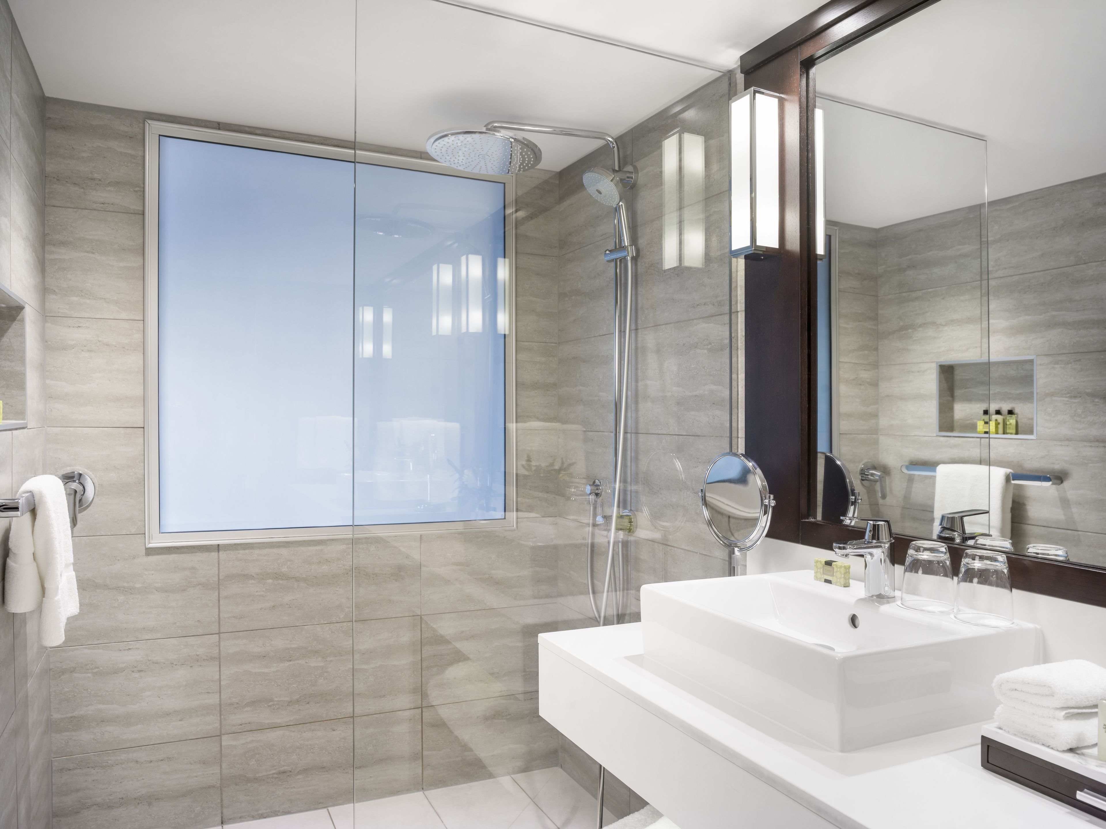 Un baño moderno con un espejo grande, cabina de ducha de vidrio y un lavabo blanco.