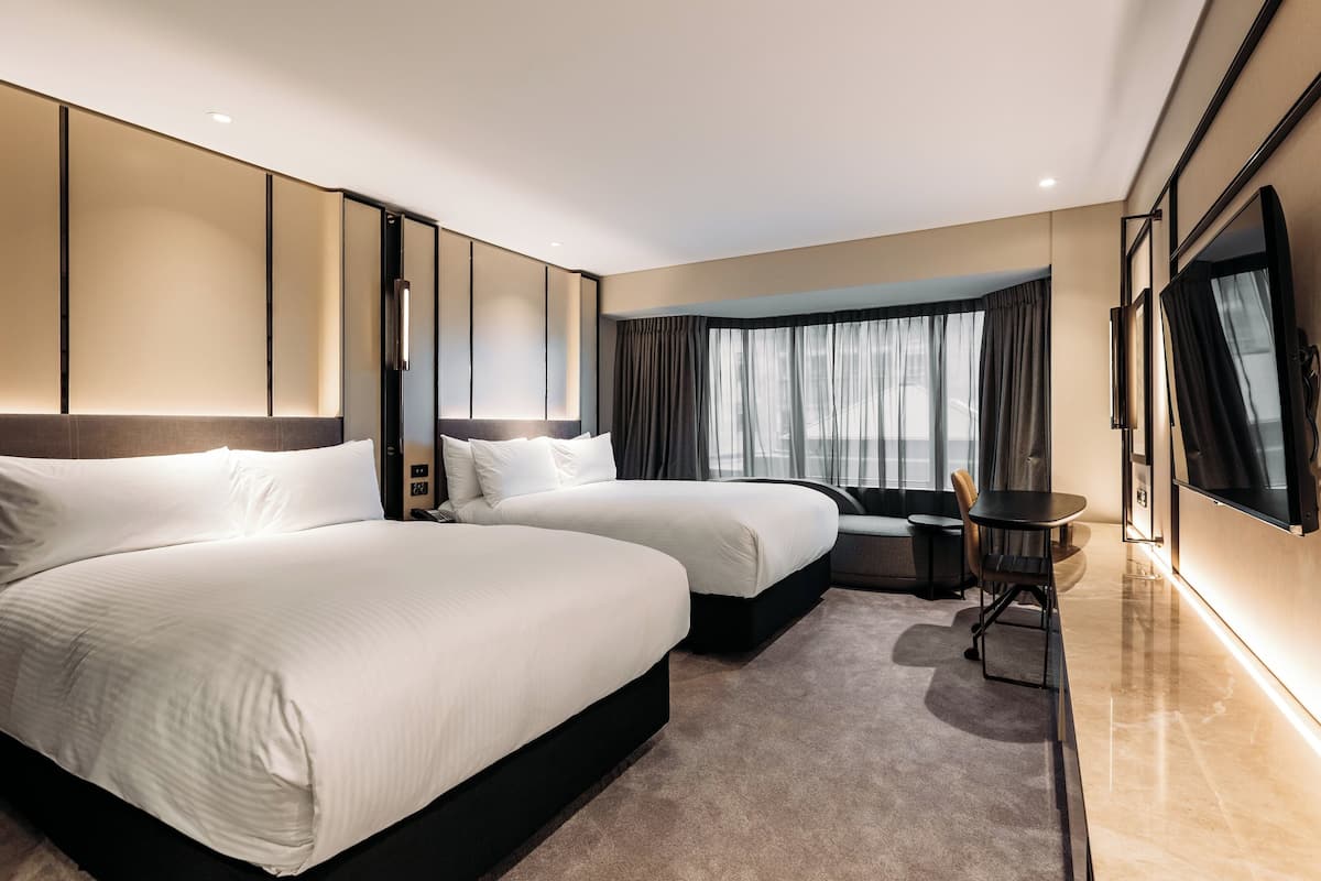 Une chambre d’hôtel moderne équipée de deux grands lits, d’un bureau, d’une chaise et d’une télévision.