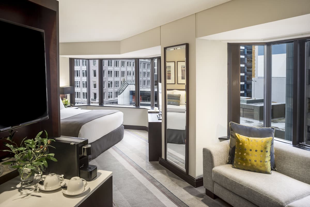 Une chambre d’hôtel équipée d’un lit, d’un canapé, d’une télévision, d’une machine à café et offrant une vue sur le paysage urbain.