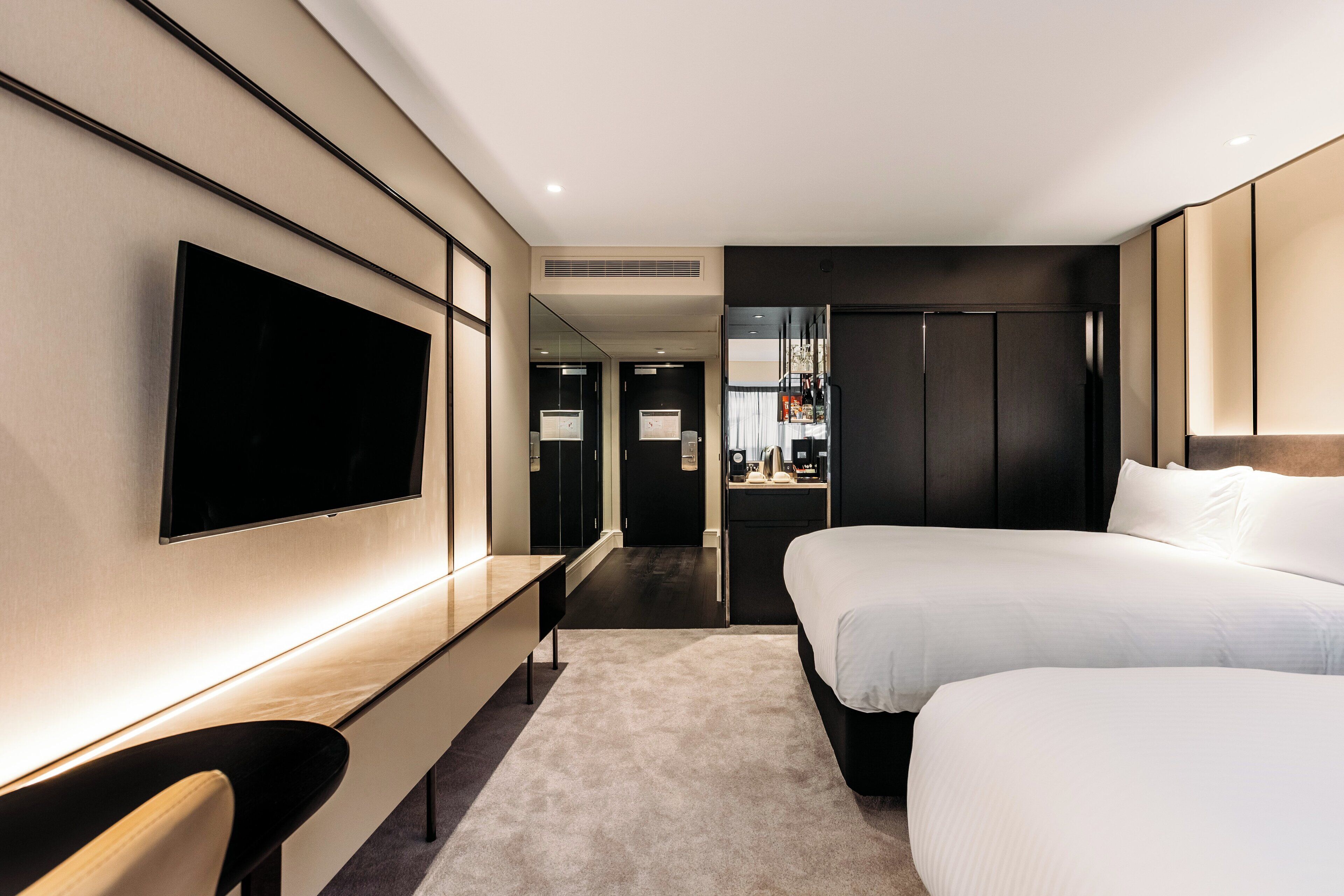 Une chambre d’hôtel moderne équipée d’un grand téléviseur à écran plat, d’un lit, d’un bureau et d’un miroir.