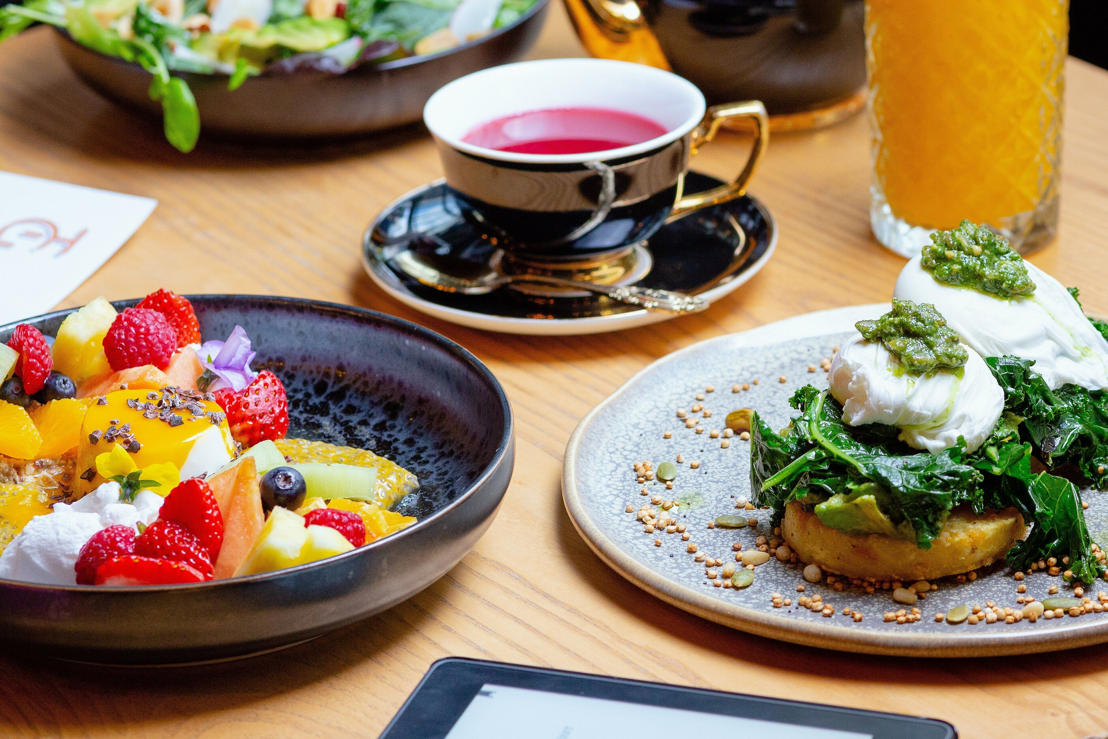 A table with a variety of dishes including a fruit salad, a dish with greens and a poached egg, and a cup of tea.
