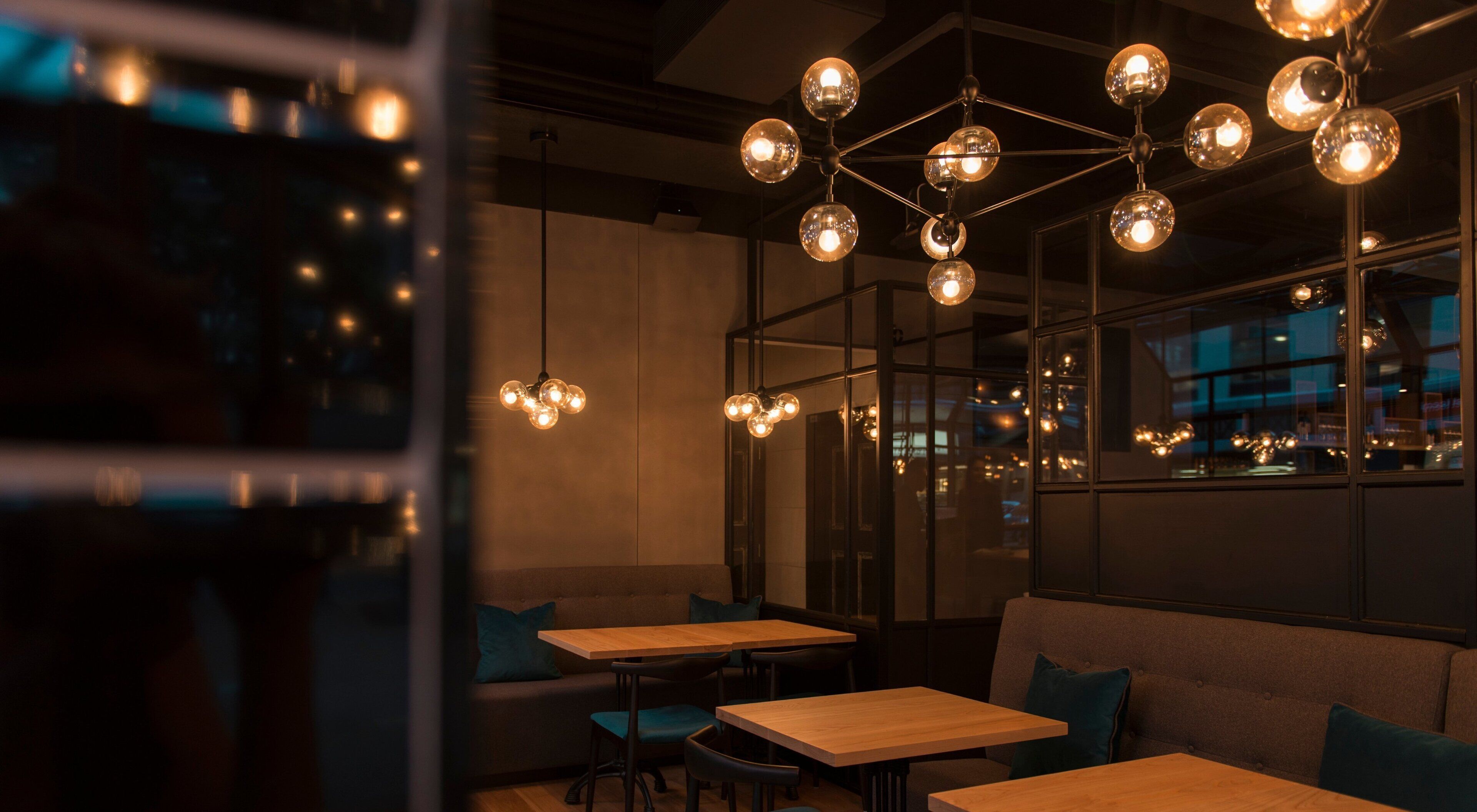 A modern interior with wooden tables and benches, a hanging spherical light fixture, and large windows.