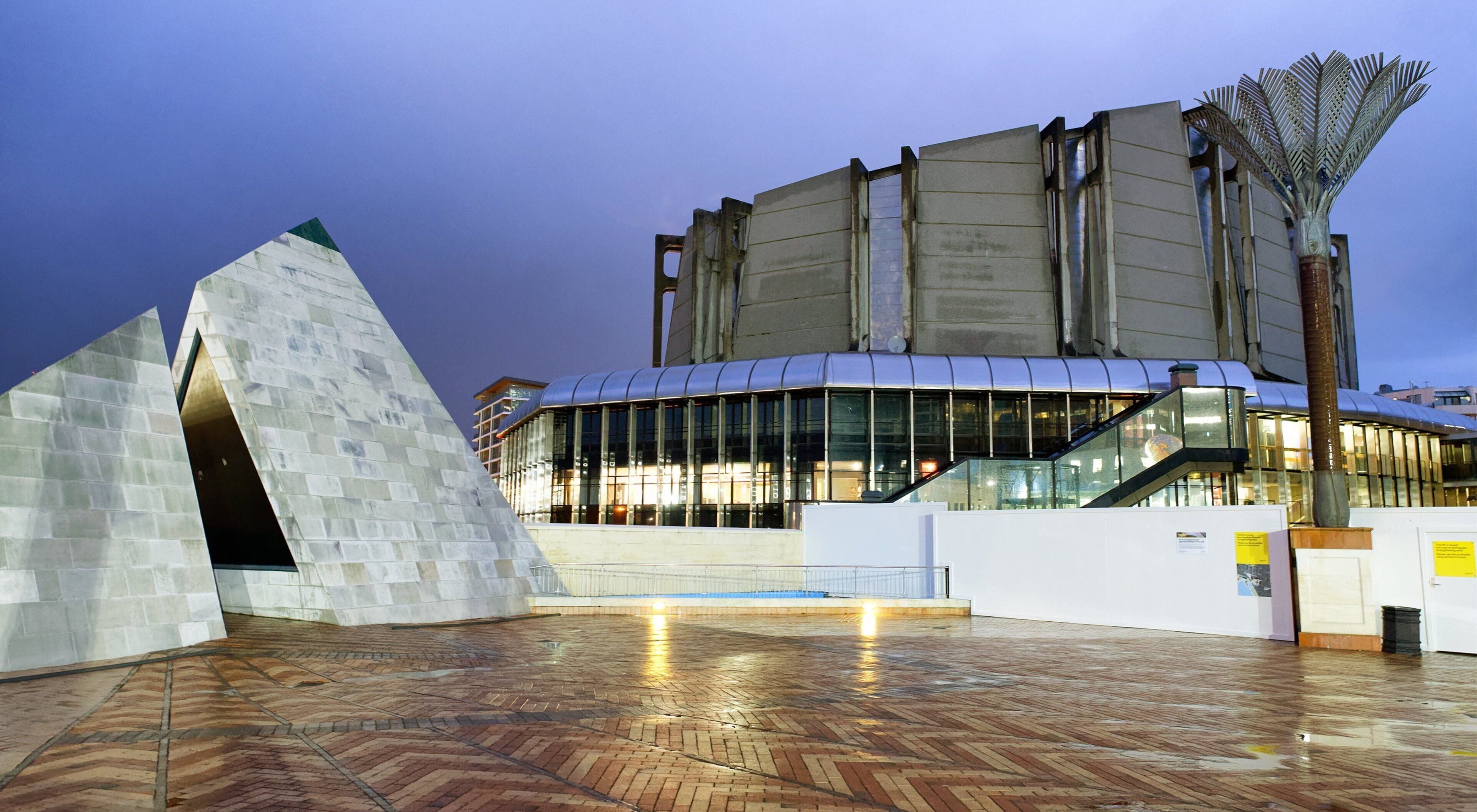 A modern building with a glass facade and a unique angular sculpture in the foreground.