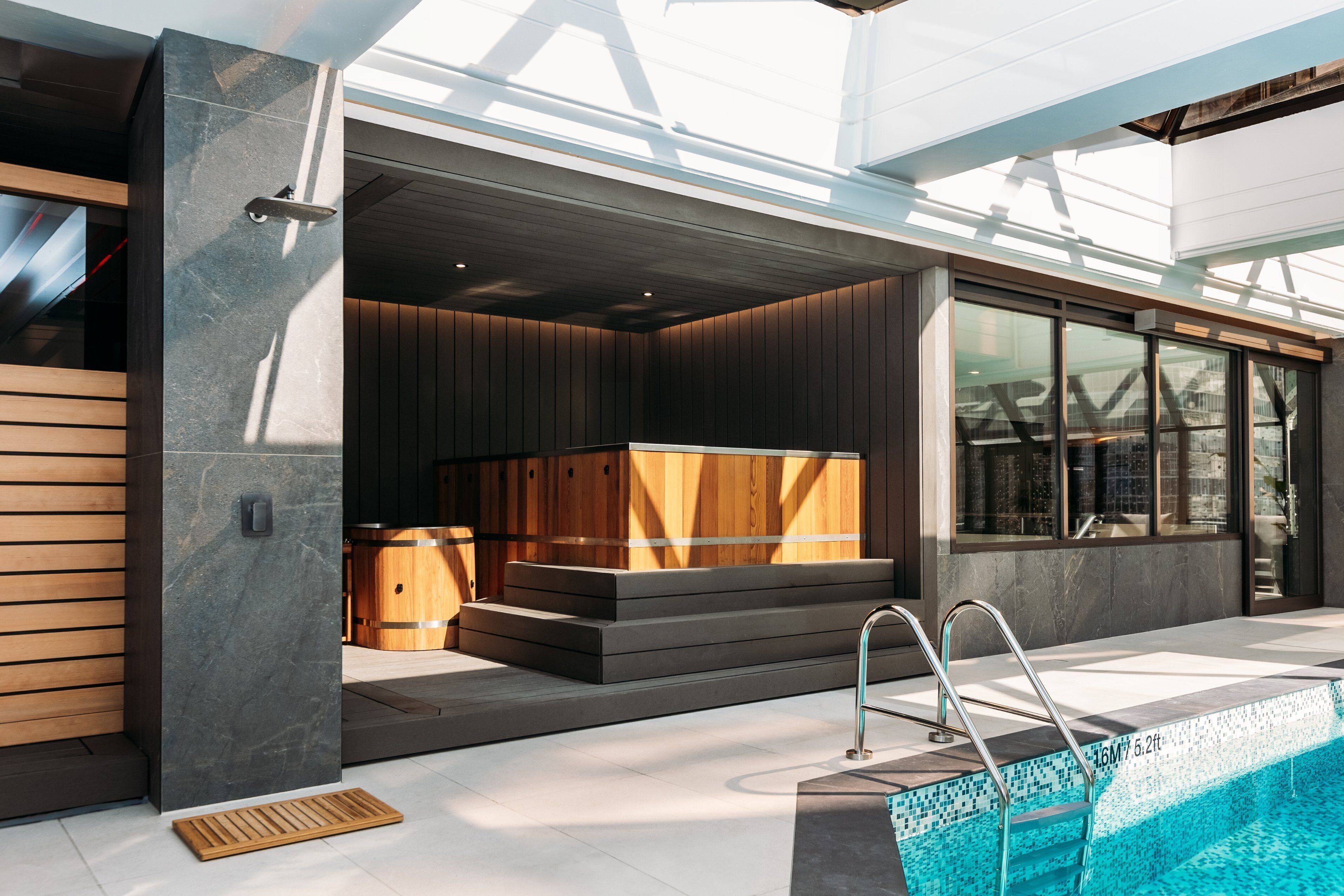 A modern outdoor pool area with a built-in sauna, a wooden bench, and a metal ladder.
