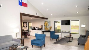A modern living room with a sofa, two armchairs, a coffee table, and a TV. There is a kitchen area in the background with a dining table and chairs.