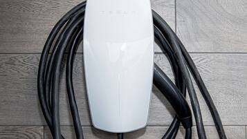 Una estación de carga Tesla blanca con varios cables de carga negros sobre un piso de madera.