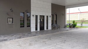A building entrance with a covered area, benches, and a paved walkway.