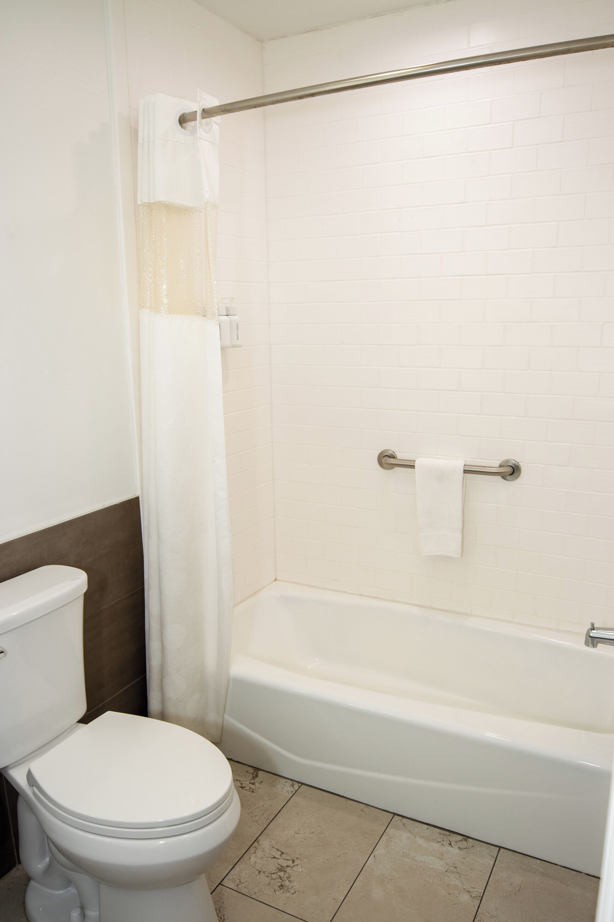 A bathroom with a toilet, a shower with a curtain, and a bathtub.