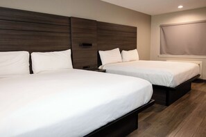Two single beds with wooden headboards, a window with a blind, and a wooden floor. - Americas Best Value Inn Harlingen (Harlingen)