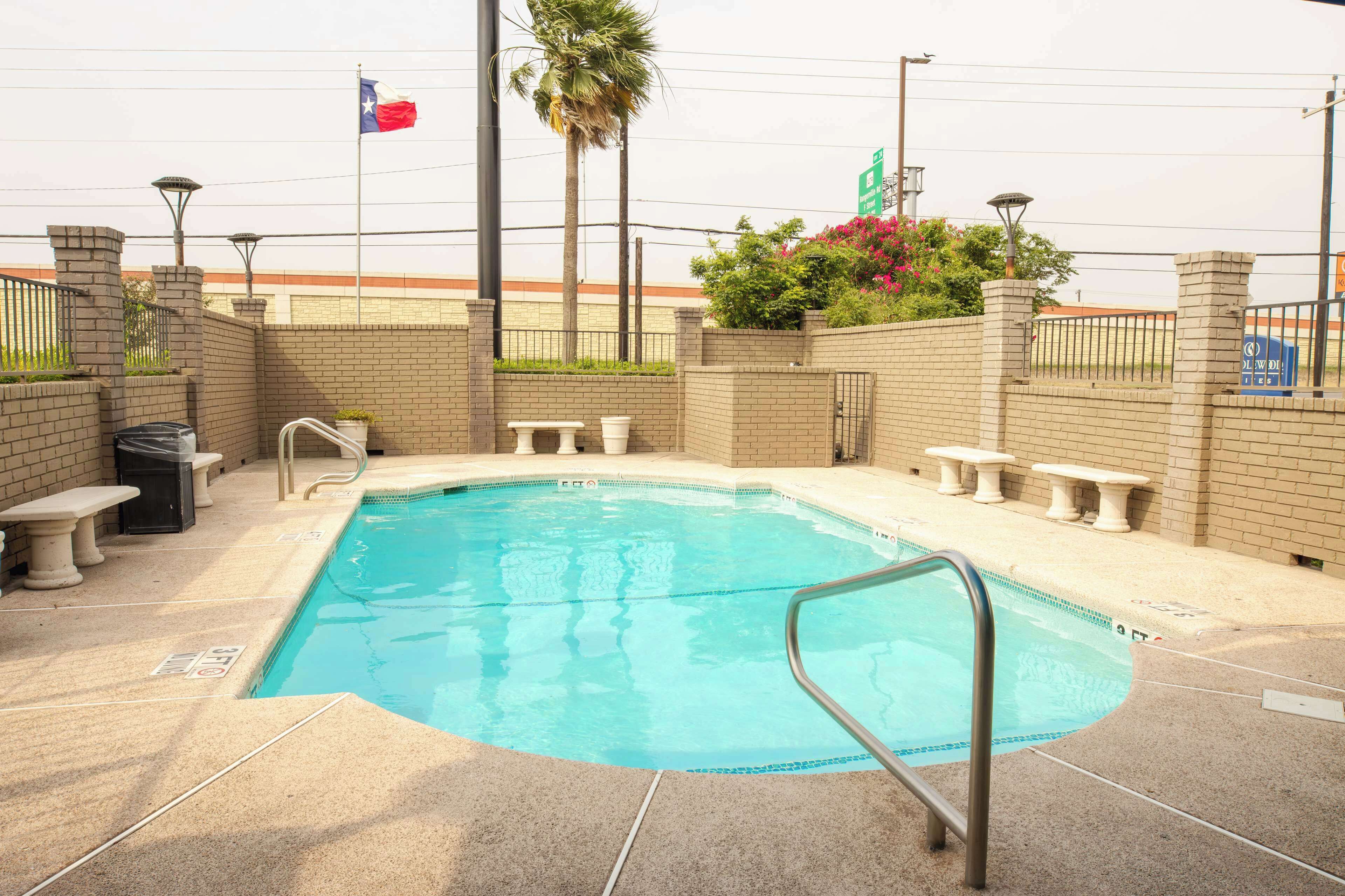 Una piscina con una escalera metálica, rodeada de muros de ladrillo y bancos.