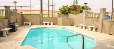 A swimming pool with a metal ladder, surrounded by brick walls and benches.