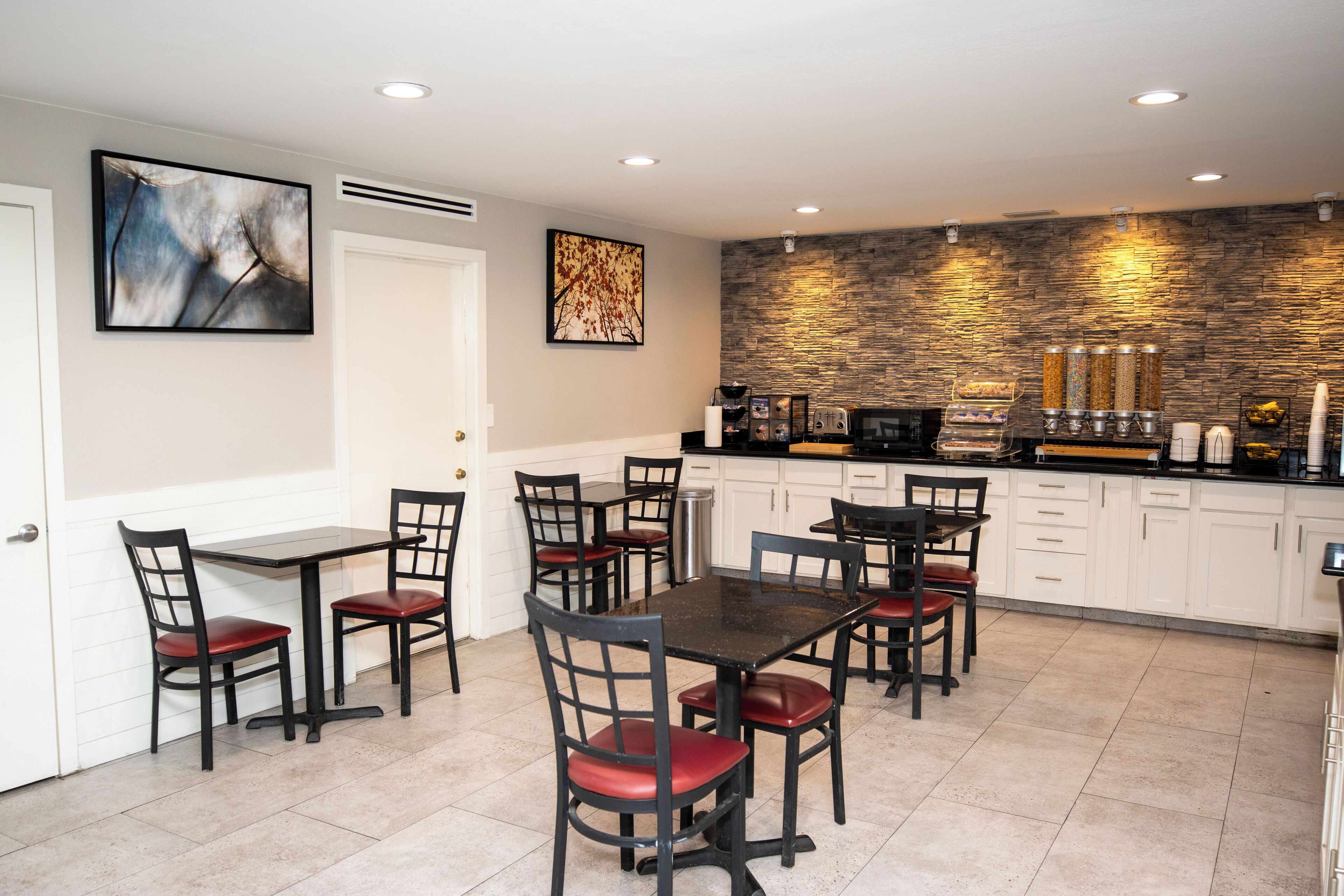 A modern kitchen with white cabinets, a stone backsplash, and a dining area with black tables and chairs.