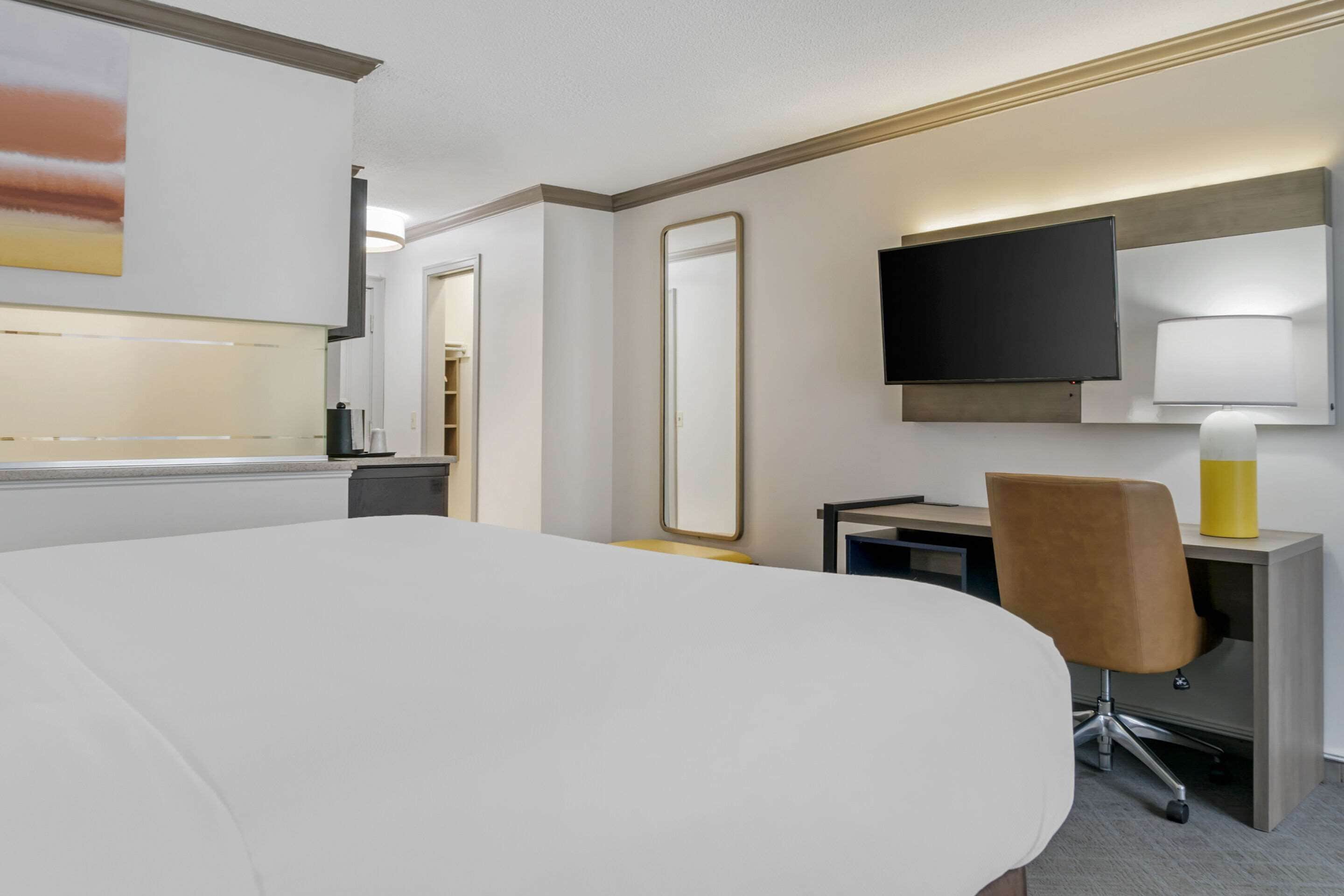 A hotel room with a large bed, a desk with a chair, a television, and a mirror.
