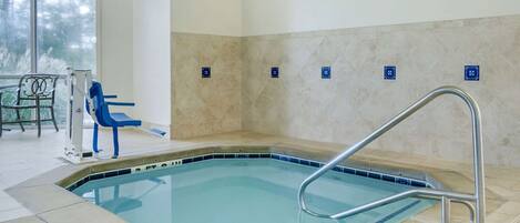 Piscina interior com escada de metal, cadeiras azuis e vista para árvores através de uma grande janela.