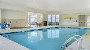 Una piscina interior con agua azul cristalina, rodeada de paredes y piso de azulejos. Se observan escaleras metálicas de piscina, y un conjunto de sillas y mesas cerca de la piscina.