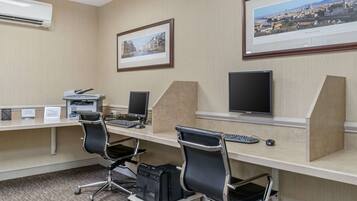 Una sala de conferencias con tres escritorios, cada uno con una computadora, teclado y ratón. Hay dos cuadros en las paredes, uno que muestra Florencia, Italia, y otro un paisaje urbano. Una unidad de aire acondicionado está instalada en la pared.