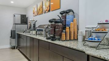 A modern kitchen with a coffee station, including coffee dispensers, a water dispenser, and a buffet area with bowls and plates.